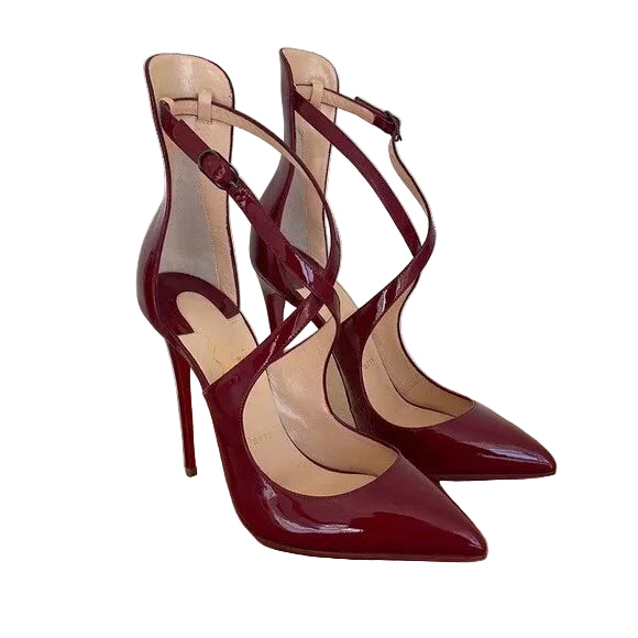 A pair of pointed-toe high-heel pumps in glossy deep burgundy patent leather, featuring crisscross ankle straps and a stiletto heel, displayed on a brown shoebox against a light off-white background.