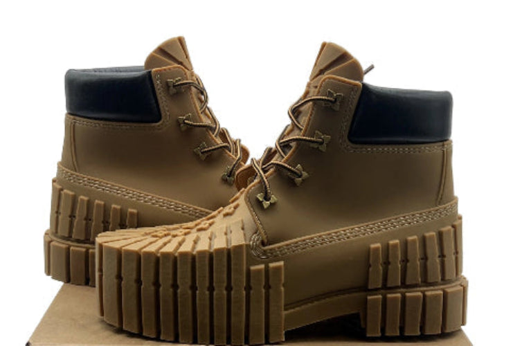 Tan boots with black soles on a cardboard box against a white background