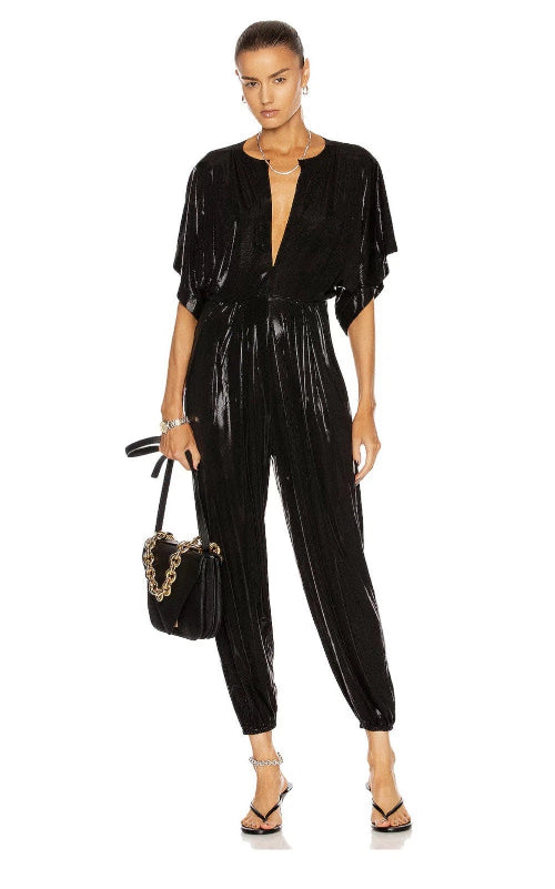 Woman wearing a black vinyl jumpsuit holding a handbag on a white background