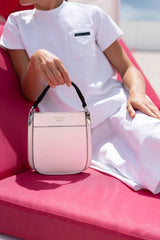 Person holding a pink handbag on a pink surface with a blurred background