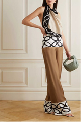 Woman wearing a stylish outfit with a patterned top, beige pants, and black and white shoes in an elegant room.