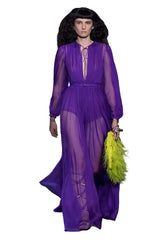 Model wearing a purple outfit with a green feathered clutch on a runway.