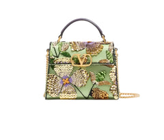 A structured light green handbag with an intricate floral and butterfly embellishment in gold, purple, and green sequins, featuring a top handle and a gold-tone chain strap, photographed against a plain white background.