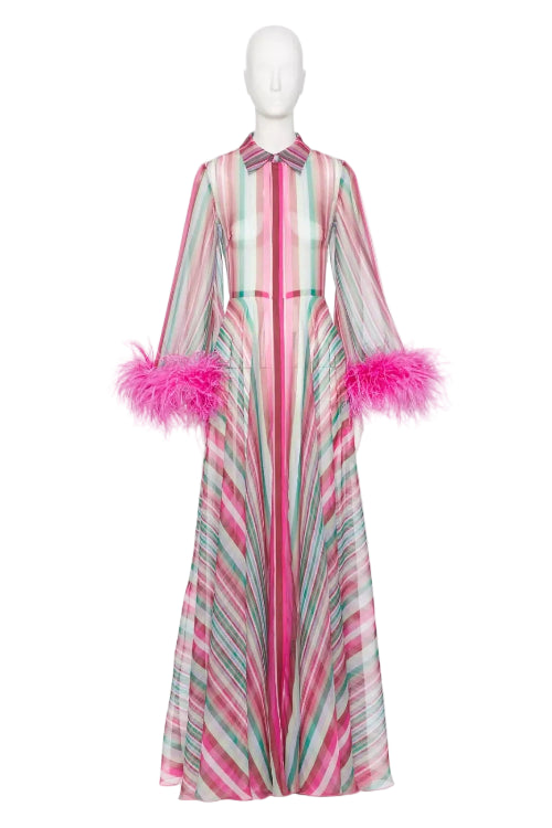 A long-sleeved maxi dress with vertical pink, mint green, and white stripes, featuring bright pink feather trim at the cuffs and a matching striped bow at the collar, displayed on a white mannequin.