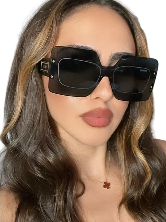 A close-up of a woman wearing oversized black square sunglasses with a thick black frame and dark lenses.