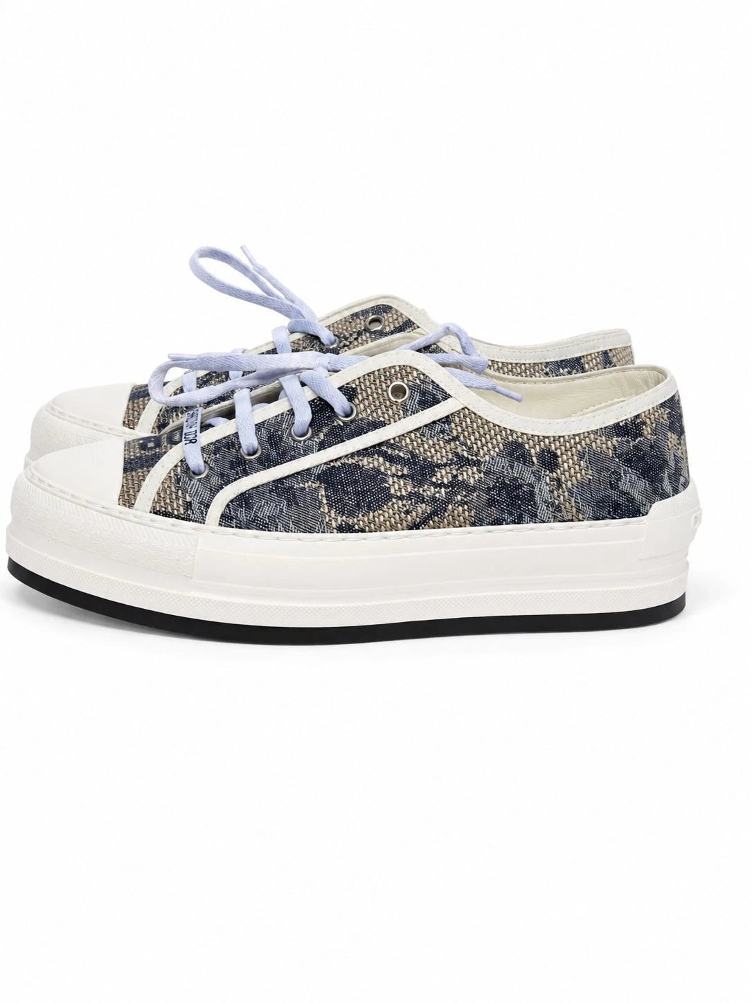 A pair of low-top platform sneakers featuring a dark blue and beige floral snakeskin pattern canvas upper, white rubber toe caps and midsoles, and light blue laces, shown against a plain white background.