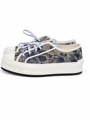 A pair of low-top platform sneakers featuring a dark blue and beige floral snakeskin pattern canvas upper, white rubber toe caps and midsoles, and light blue laces, shown against a plain white background.
