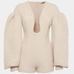A cream-colored quilted jumpsuit with long puffed sleeves, a deep V-neckline, and a front zipper, shown against a light gray background.