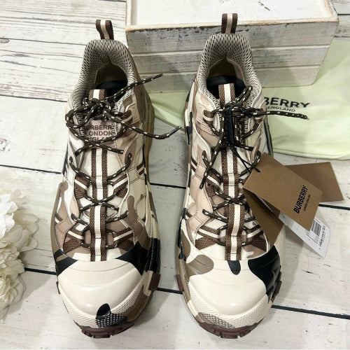 Pair of camouflage-patterned boots with a Burberry tag on a wooden surface.