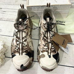 Pair of camouflage-patterned boots with a Burberry tag on a wooden surface.