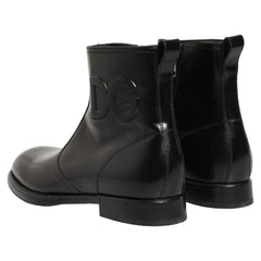 A pair of glossy black leather Chelsea-style boots with a large embossed 'DG' logo on the side, shown against a plain white background.
