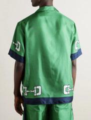 Green satin shirt with brand logos on sleeves and back, worn by a person.