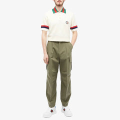 Person wearing a cream polo shirt with red and green accents and olive green cargo pants on a white background