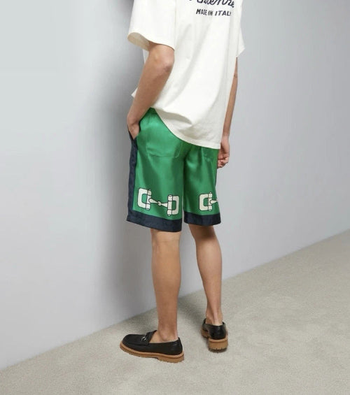Person wearing green shorts with a logo and a white t-shirt against a plain background