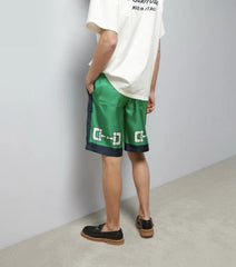 Person wearing green shorts with a logo and a white t-shirt against a plain background