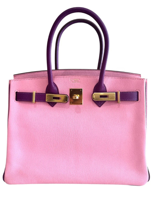 Pink handbag with purple handles and gold hardware on a white background