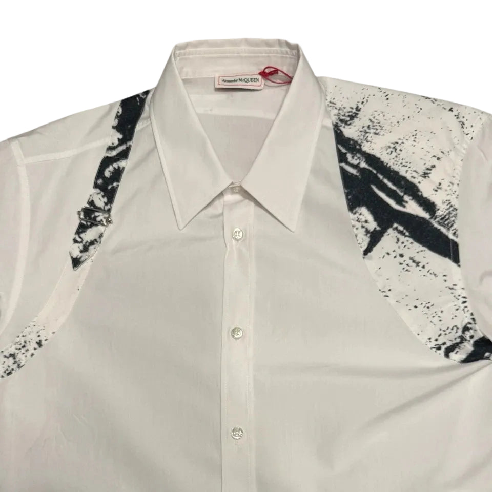 A men's long-sleeve button-up shirt in off-white with black abstract brushstroke patterns on the shoulders and upper sleeves, shown laid flat against a light gray background.