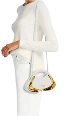 A model wearing a white ribbed knit long-sleeve top and white pants, holding a gold metallic heart-shaped accessory.
