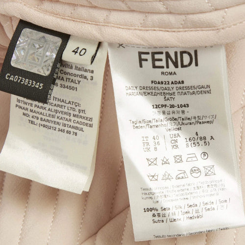 Close-up of a Fendi garment tag attached to a light pink quilted fabric, showing the Fendi Roma branding and care instructions.