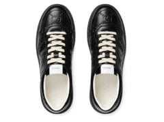 A pair of black leather Gucci sneakers shown from a top-down view on a white background. The shoes feature embossed GG logos on the toe, white laces, and a white Gucci label on the tongue.