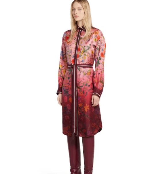 A model wearing a long-sleeved, knee-length floral print coat with a matching tie belt, paired with dark red leather boots, against a plain white background.