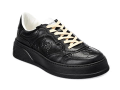 A black leather low-top sneaker with black laces and a thick black sole, shown against a plain white background.