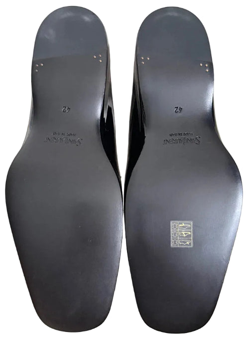 The soles of a pair of black pointed-toe pumps, showing the brand name 'SILKSTUDY' and size '42' printed on the bottom, resting on a beige carpet.