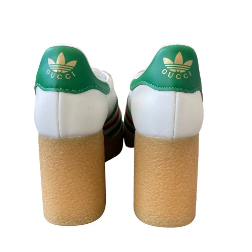 A pair of Gucci x Adidas platform sneakers shown from the back, featuring green leather heel tabs with gold logos, white leather sides, and a thick tan textured platform sole.