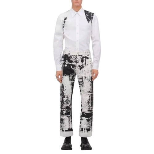 A model wearing a white long-sleeve shirt with black shoulder patches and black-and-white patterned trousers, standing against a plain white background.