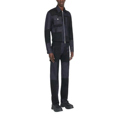 A model wearing a dark patchwork denim jacket and matching pants with a silver zipper, photographed against a light gray studio background.