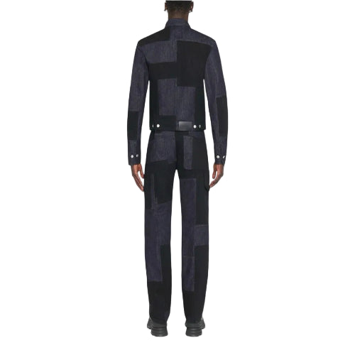 A model shown from the back wearing a dark patchwork suit with a high collar, long sleeves, and a matching belt, set against a solid light gray background.