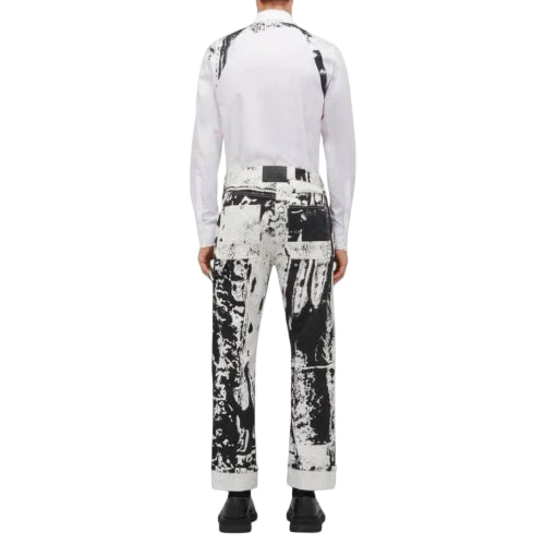 A model shown from the back wearing a white long-sleeve shirt and black-and-white abstract print trousers, paired with black shoes, against a light gray background.