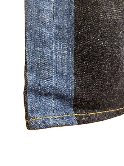 Close-up of a denim garment corner showing two fabric panels in blue and dark charcoal gray with yellow contrast stitching, on a white background.