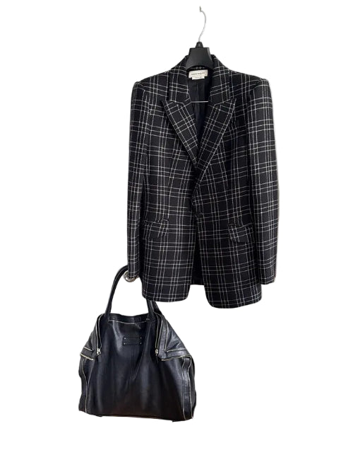 A black and gray plaid blazer jacket hanging on a hanger next to a black leather handbag, set against a white paneled door background.