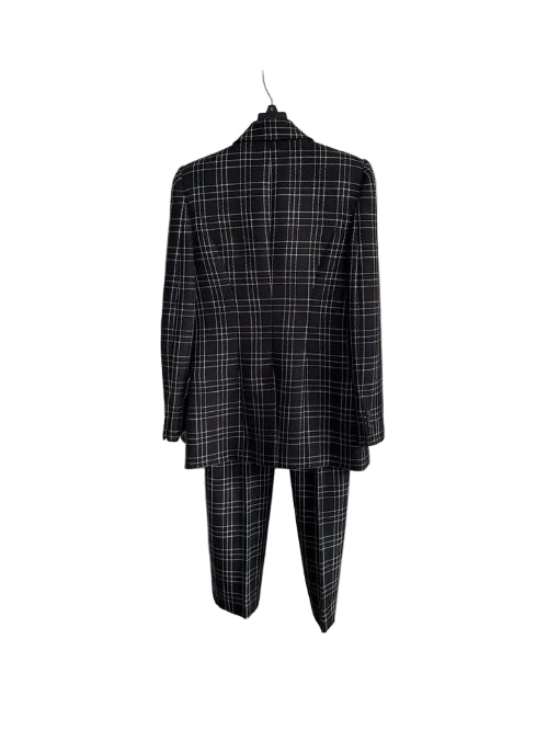 A black and white plaid suit jacket and matching trousers hanging on a hanger against a white interior door.