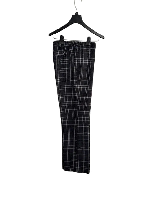 Black and white plaid cropped pants hanging on a black hanger against a white paneled door.