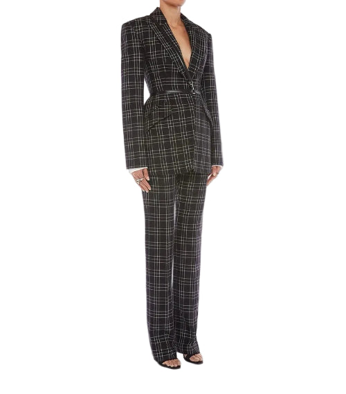 A model wearing a black and white plaid two-piece suit with a structured blazer and matching wide-leg trousers, styled with black strappy heels against a light gray studio background.