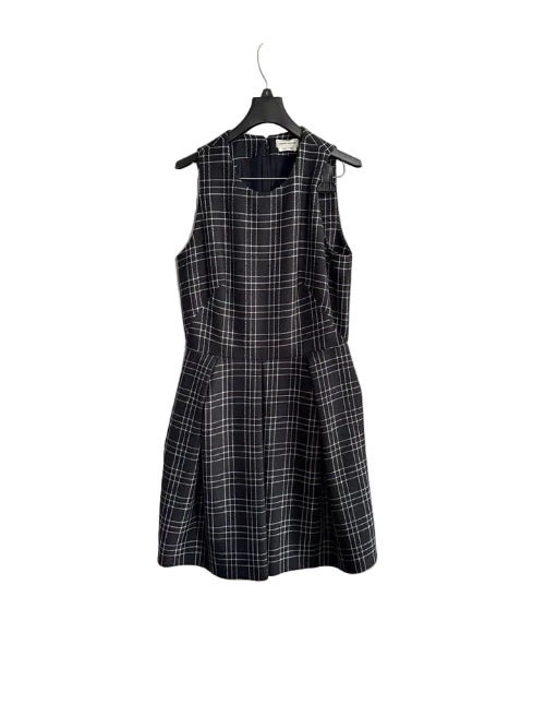 A sleeveless black and gray plaid dress hanging on a black hanger against a white paneled door.