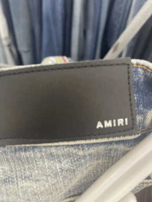 A black rectangular AMIR portable speaker with a glossy finish, resting on a gray textured fabric surface.