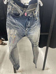 Light-wash blue distressed denim jeans with colorful embroidered details on the left leg, hanging on a display stand in a store.