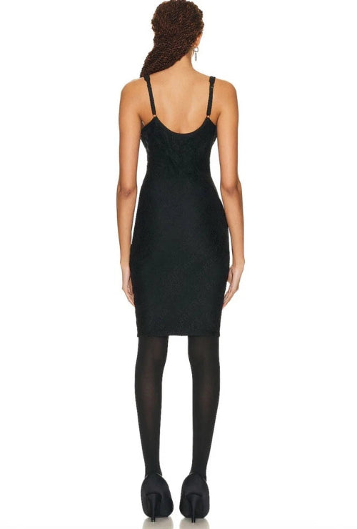 A woman shown from the back wearing a black sleeveless bodycon mini dress with thin straps, black tights, and black high heels against a plain white background.