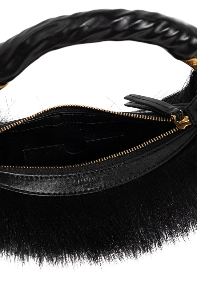Black faux-fur shoulder bag with a braided black strap and gold-tone zipper detail, shown close-up against a dark background.