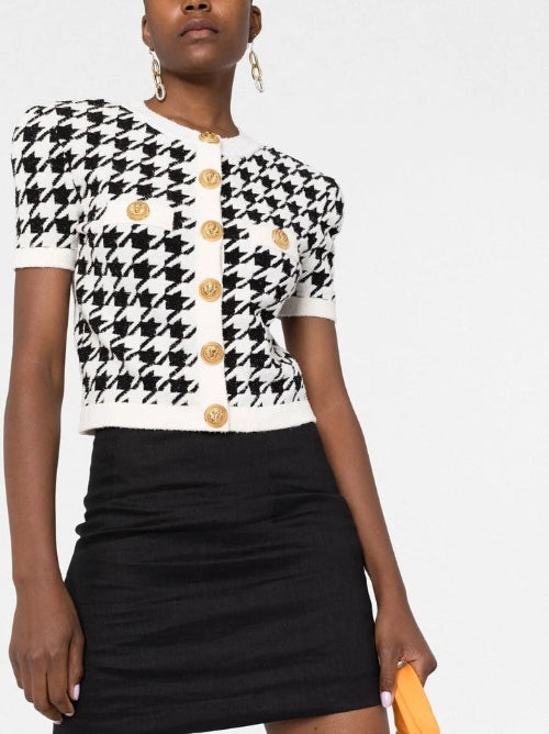 Woman wearing a black and white checkered top with gold buttons and a black skirt on a white background