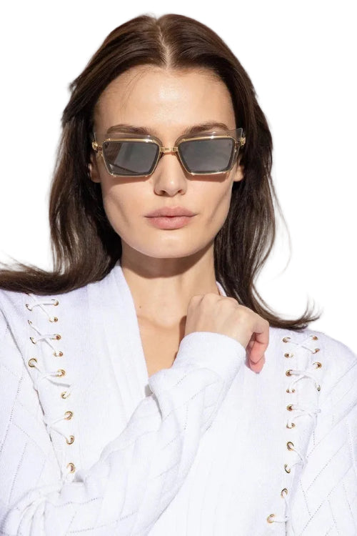 Woman wearing gold-framed sunglasses and a white outfit with gold accents.