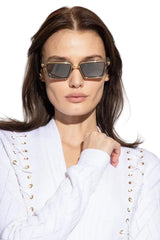 Woman wearing gold-framed sunglasses and a white outfit with gold accents.