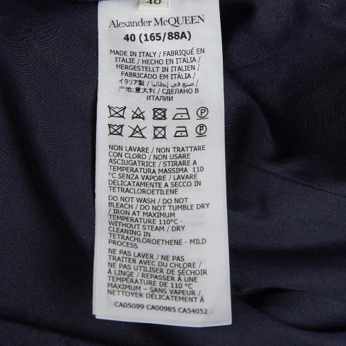 A close-up of a white garment care label for Alexander McQueen, showing the brand name and washing instructions printed in black text on a dark navy or black fabric background.
