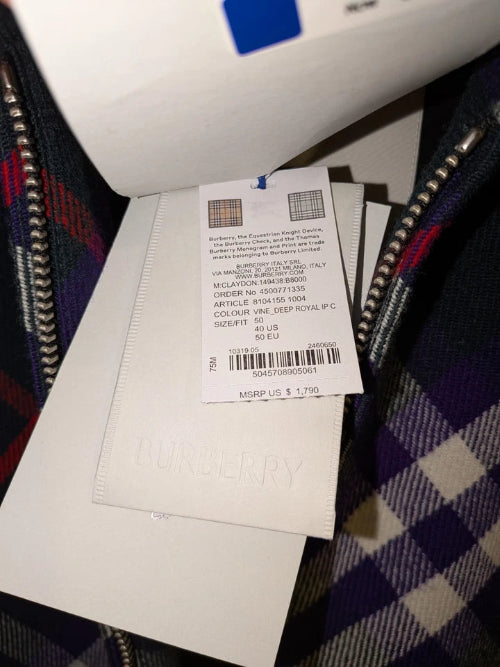 A close-up of a white rectangular product, likely a notebook, journal, or card album, with a black and white striped spine and a small attached shipping label, set against a dark plaid fabric background.