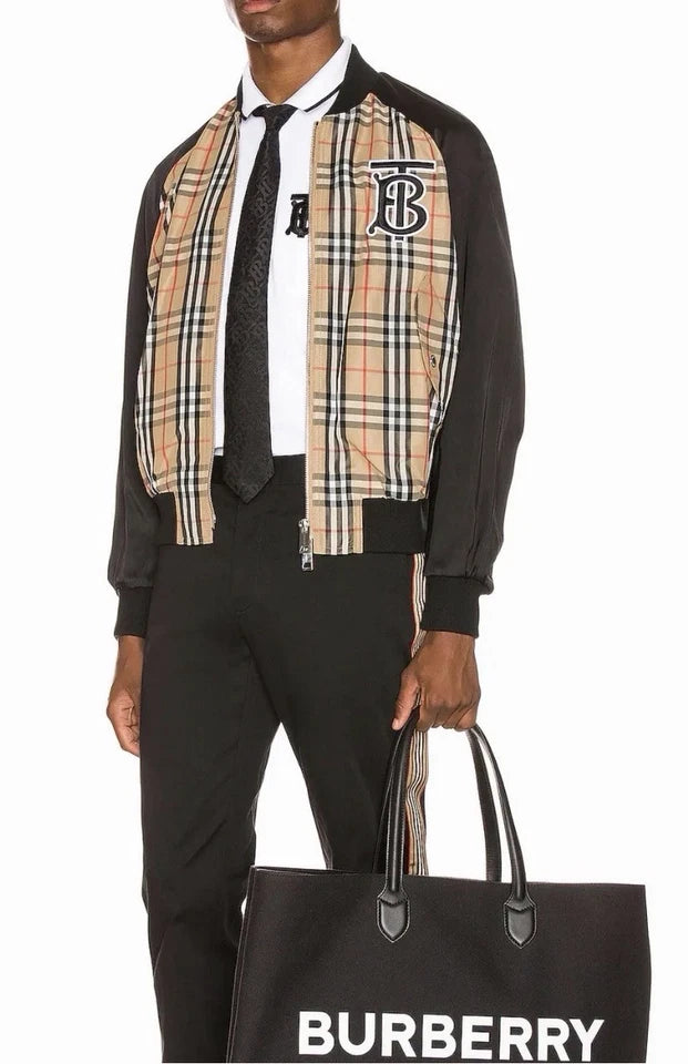 A man wearing a Burberry check jacket over a black shirt and trousers, holding a black Burberry shopping bag with the brand name in white text.