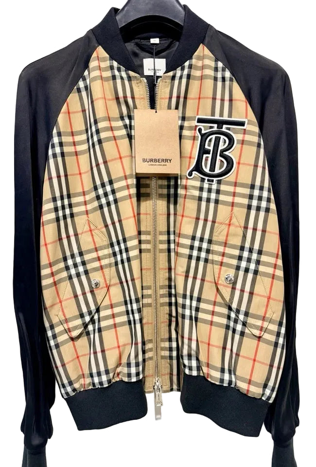 A Burberry zip-up bomber jacket with black ribbed sleeves, collar, and hem, featuring a beige plaid body with red and blue check lines and a large embroidered Burberry logo on the chest.