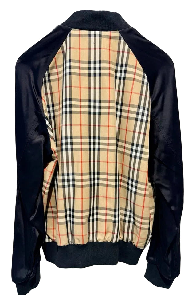 A vintage Burberry-style plaid jacket with black satin sleeves and collar, featuring a beige plaid body with red and navy check lines, hanging on a black hanger against a white door.